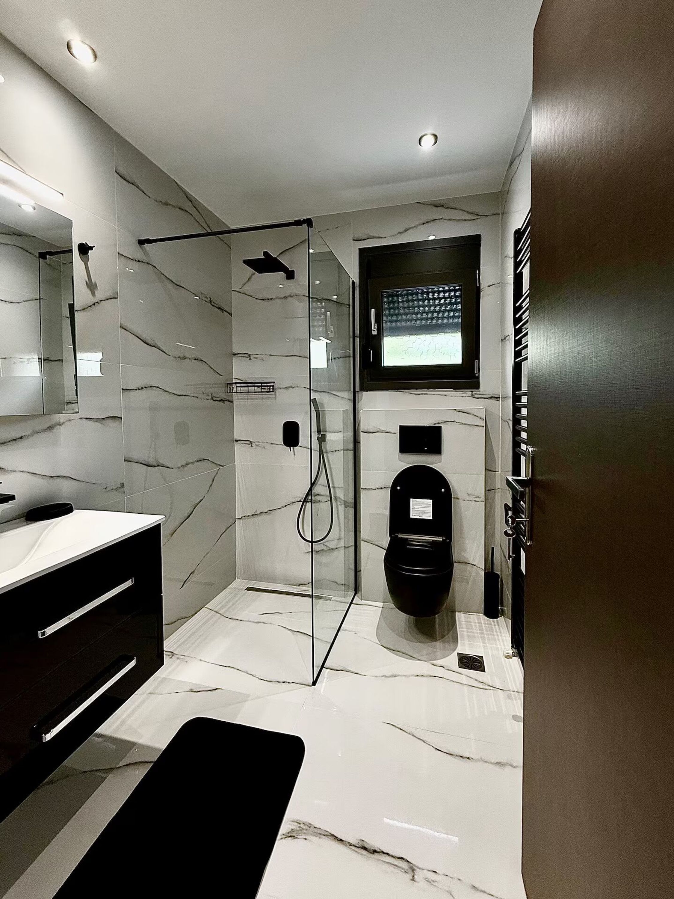 A modern bathroom with a glass-enclosed shower, a black toilet, and a vanity with a mirror.