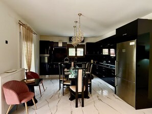 A modern kitchen with a dining area, marble flooring, and a chandelier. - Moonlit Olives - Corfu Luxurious Stylish Escape (Corfu)