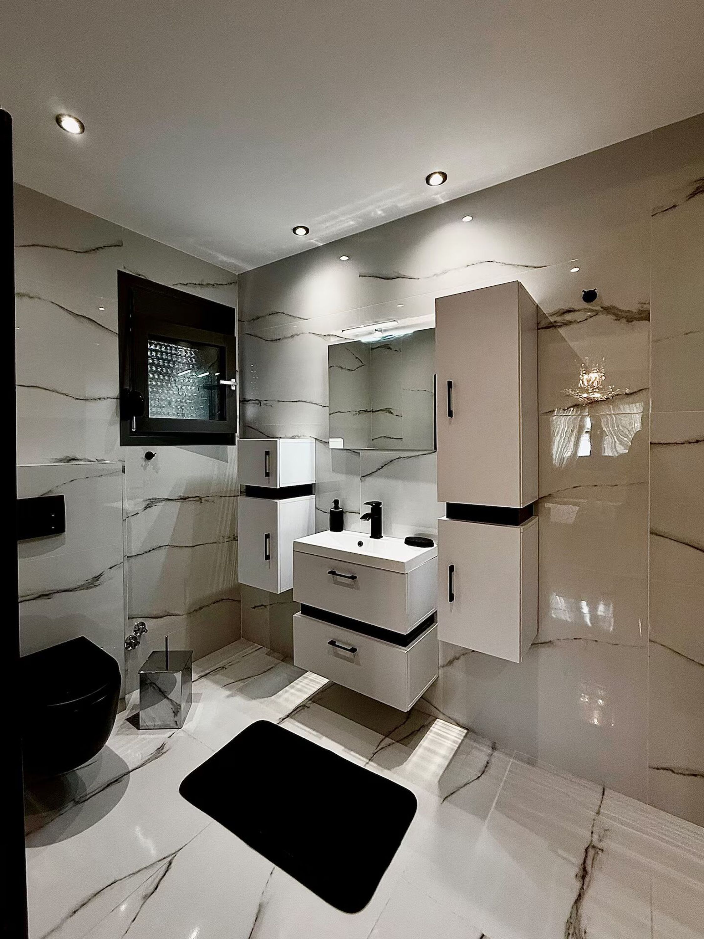 A modern bathroom with a marble floor, a black sink, a mirror, and a window.