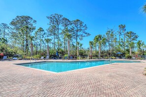 A rectangular swimming pool with a brick deck, surrounded by tall trees and lounge chairs.