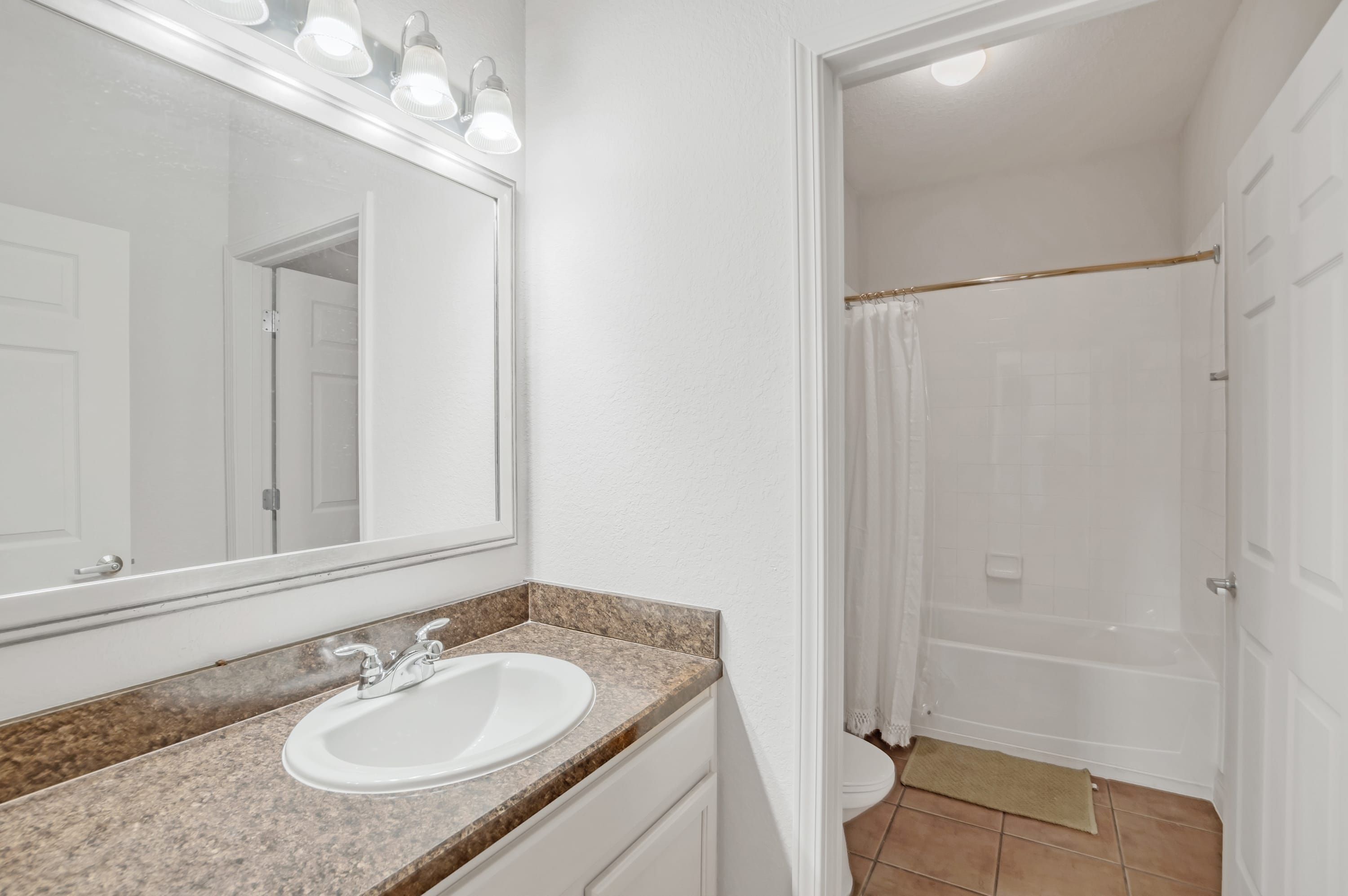 Un baño con lavamanos blanco, un espejo y zona de ducha.