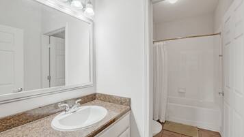 Un baño con lavamanos blanco, un espejo y zona de ducha.