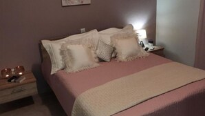 Un dormitorio con cama, almohadas, una mesita de noche con lámpara y un cuadro en la pared.