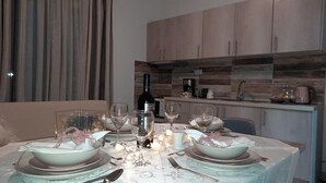 Comedor con una mesa preparada para cuatro, una botella de vino y una cocina al fondo.