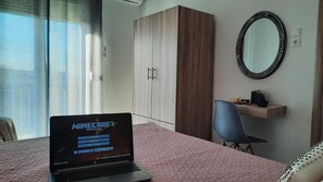 Een slaapkamer met een bed, een laptop waarop een spel wordt weergegeven, een kledingkast, een stoel en een spiegel aan de muur.