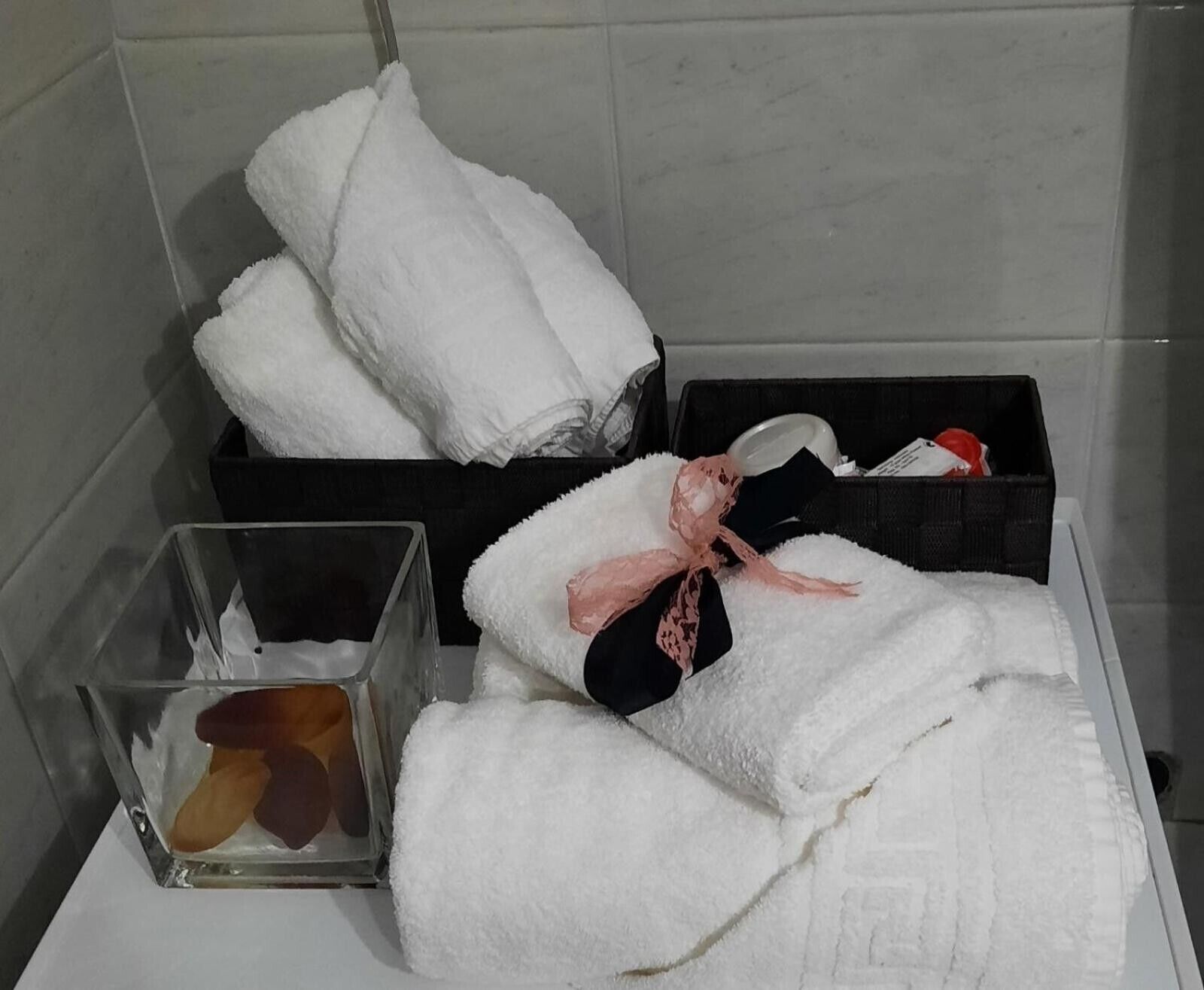 A bathroom with white towels, a glass container with a brown object, and a black box with toiletries.