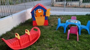 A children's play area with a slide, a small house, and plastic chairs. - Apartment 'Chrissi Princess 1' with Private Garden, Wi-Fi and Air Conditioning (Skala Sotiros)