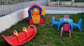 Ein Spielbereich für Kinder mit einer Rutsche, einem kleinen Haus und Plastikstühlen.
