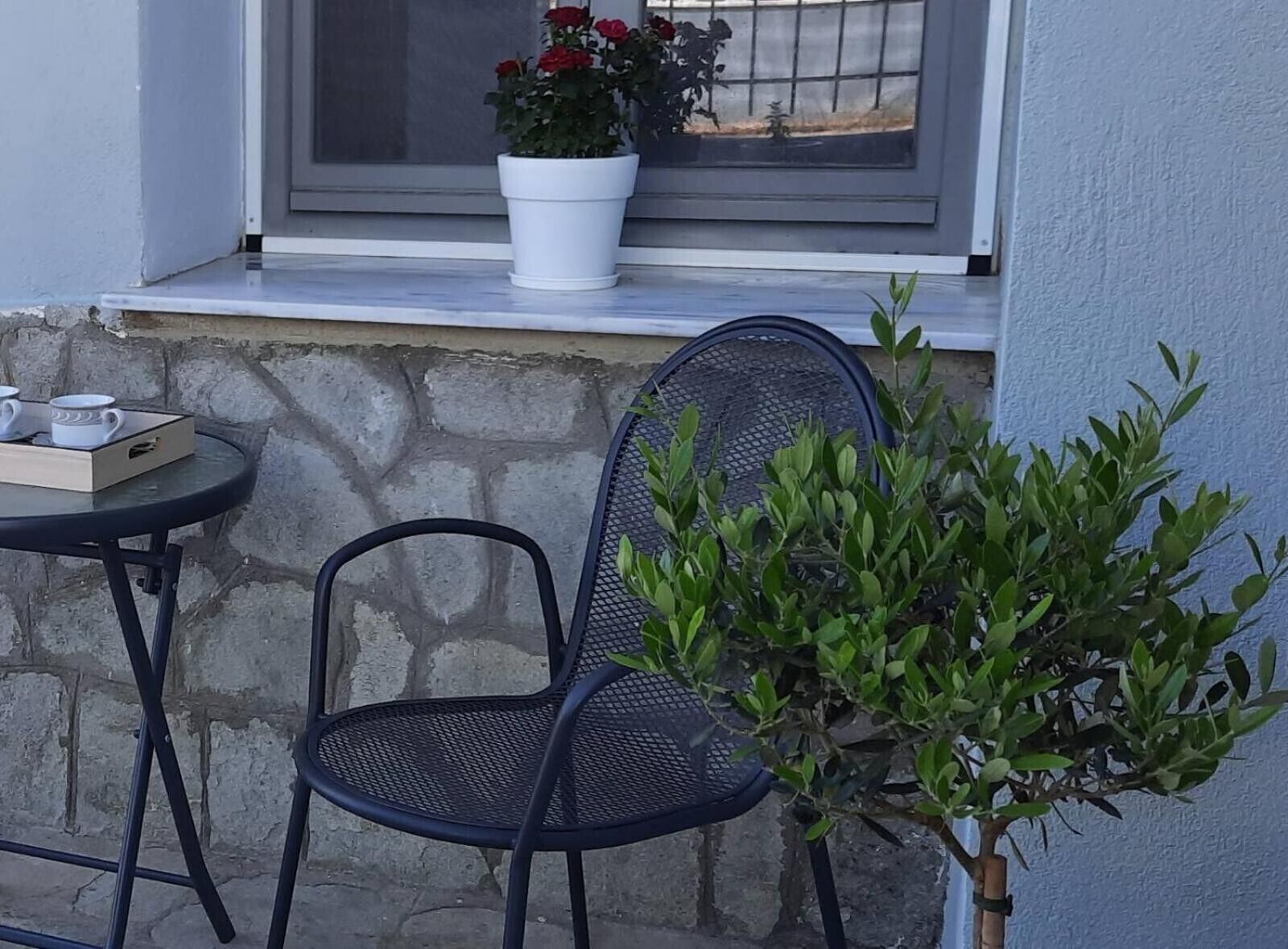 Un patio con una mesa y sillas, una planta en maceta y una ventana con vistas.