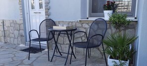 Ein kleiner Sitzbereich im Freien mit Tisch und zwei Stühlen, einem Blumentopf und einem Fenster mit Blick.