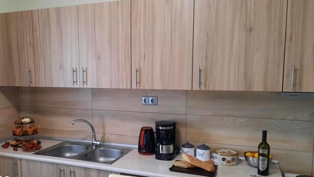 A kitchen with wooden cabinets, a stainless steel sink, a coffee maker, a bread loaf, a bottle of wine, and a bowl of fruit. - Apartment 'Chrissi Princess 1' with Private Garden, Wi-Fi and Air Conditioning (Skala Sotiros)