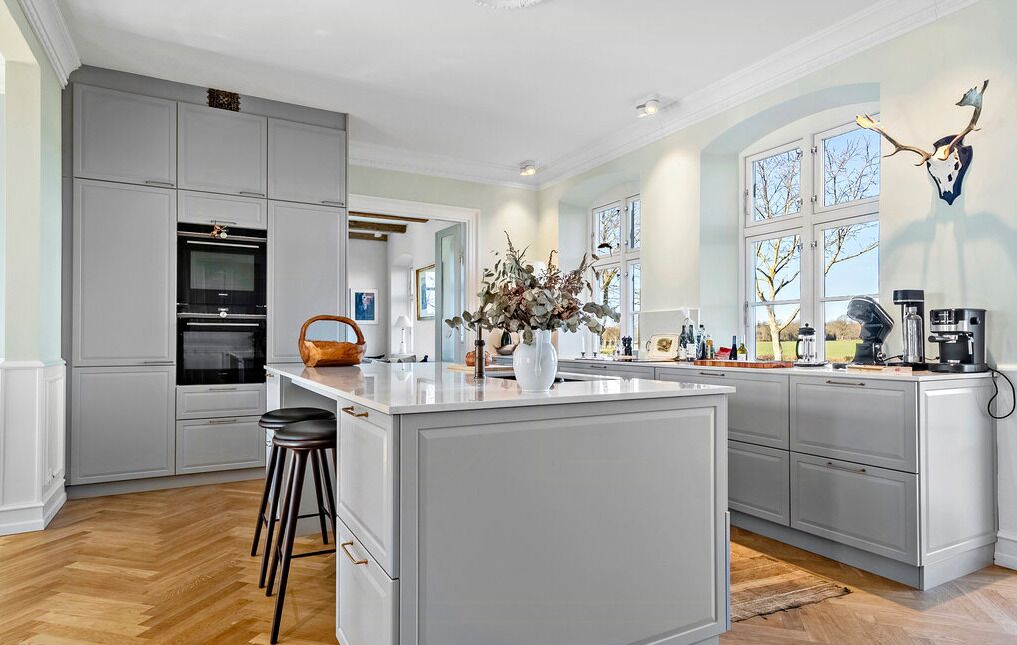A modern kitchen with grey cabinetry, a central island, and a large window providing natural light.