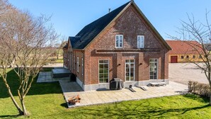 A brick house with a sloped roof, a patio with outdoor furniture, and a lawn. - Renovated farmhouse with views over Lillebælt (Sønder Stenderup)