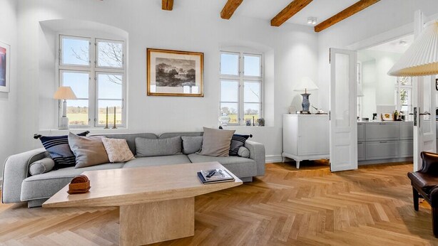 A spacious living room with a large sofa, a coffee table, and a view of the outdoors through large windows. - Renovated farmhouse with views over Lillebælt (Sønder Stenderup)
