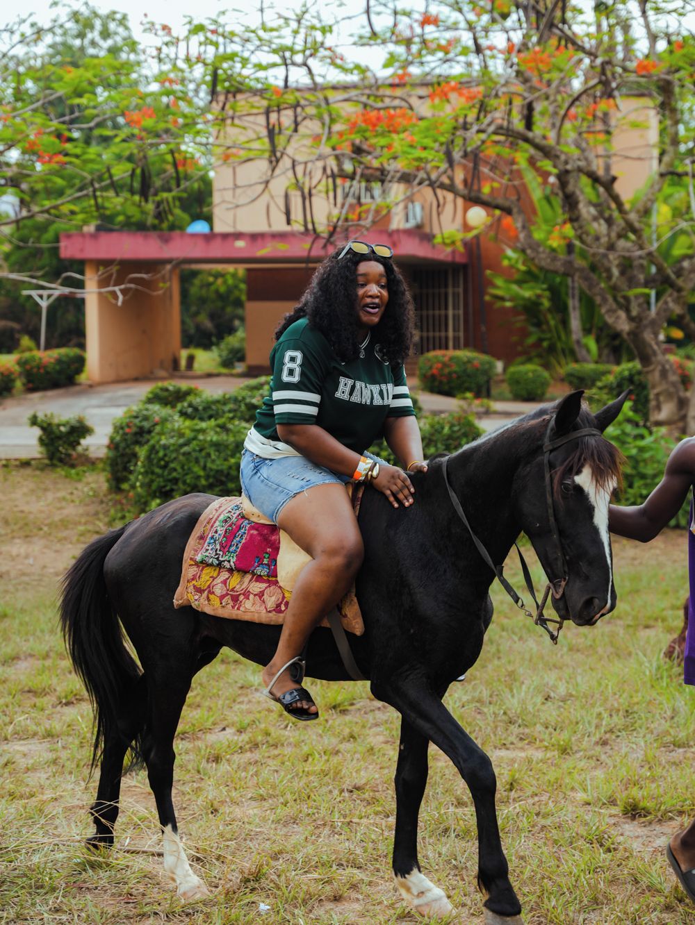 A person riding a horse in a grassy area with a building in the background.