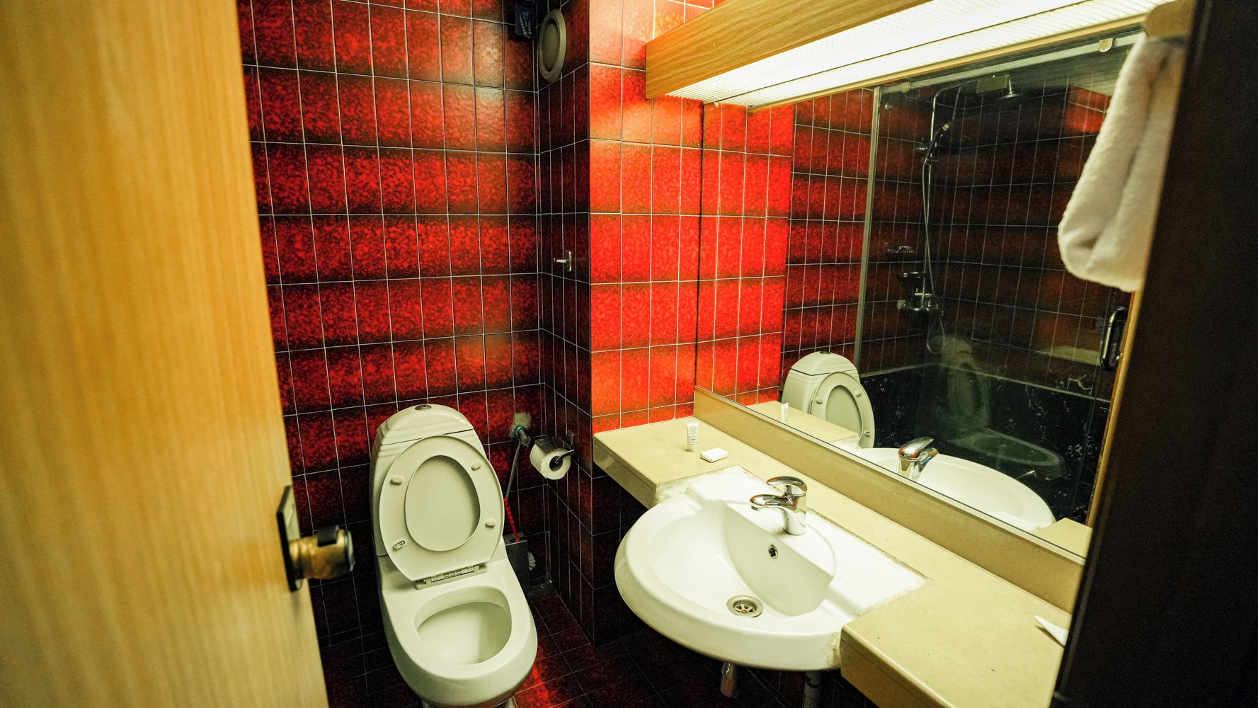 A bathroom with red tiled walls, a white toilet, a sink, and a mirror.