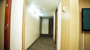 A hotel hallway with carpeted flooring, wooden doors, and a wall-mounted television.