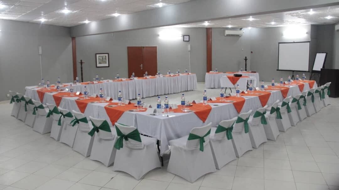 Un salón de conferencias con mesas redondas, sillas blancas y manteles naranjas.