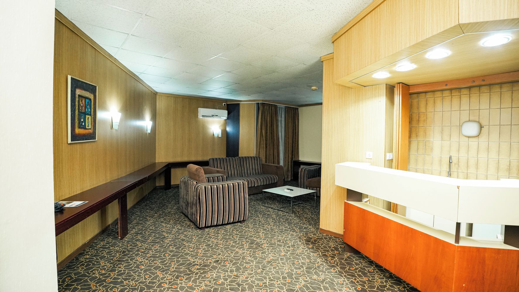 Quarto de hotel com sofá, mesa pequena, banco e banheiro com pia e espelho.