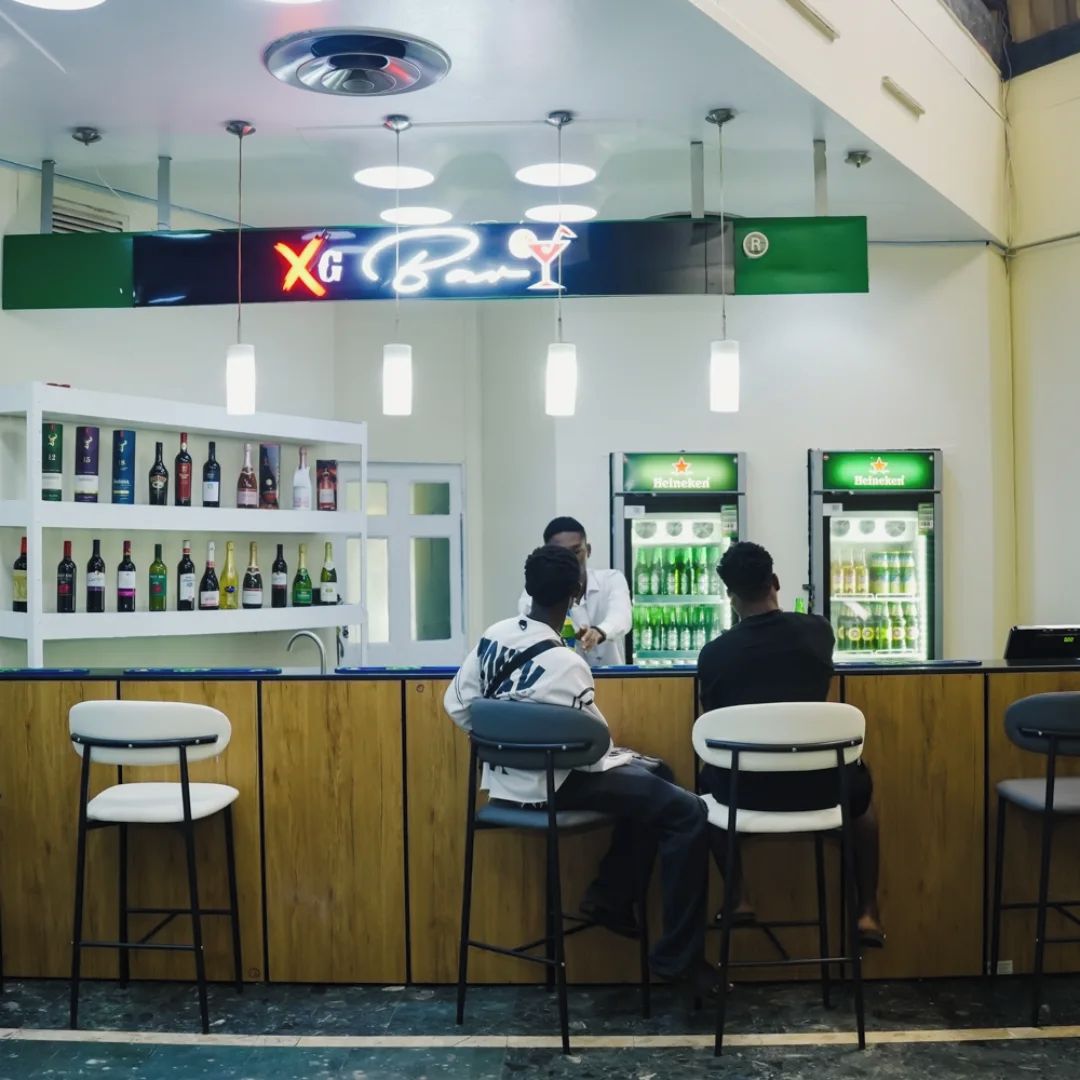 A bar area with a neon sign, shelves of bottled beverages, and two refrigerators stocked with drinks.