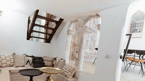 Un soggiorno con parete in pietra, un divano con cuscini decorati, un tavolino con un vaso dorato e una scala che conduce a un altro livello.