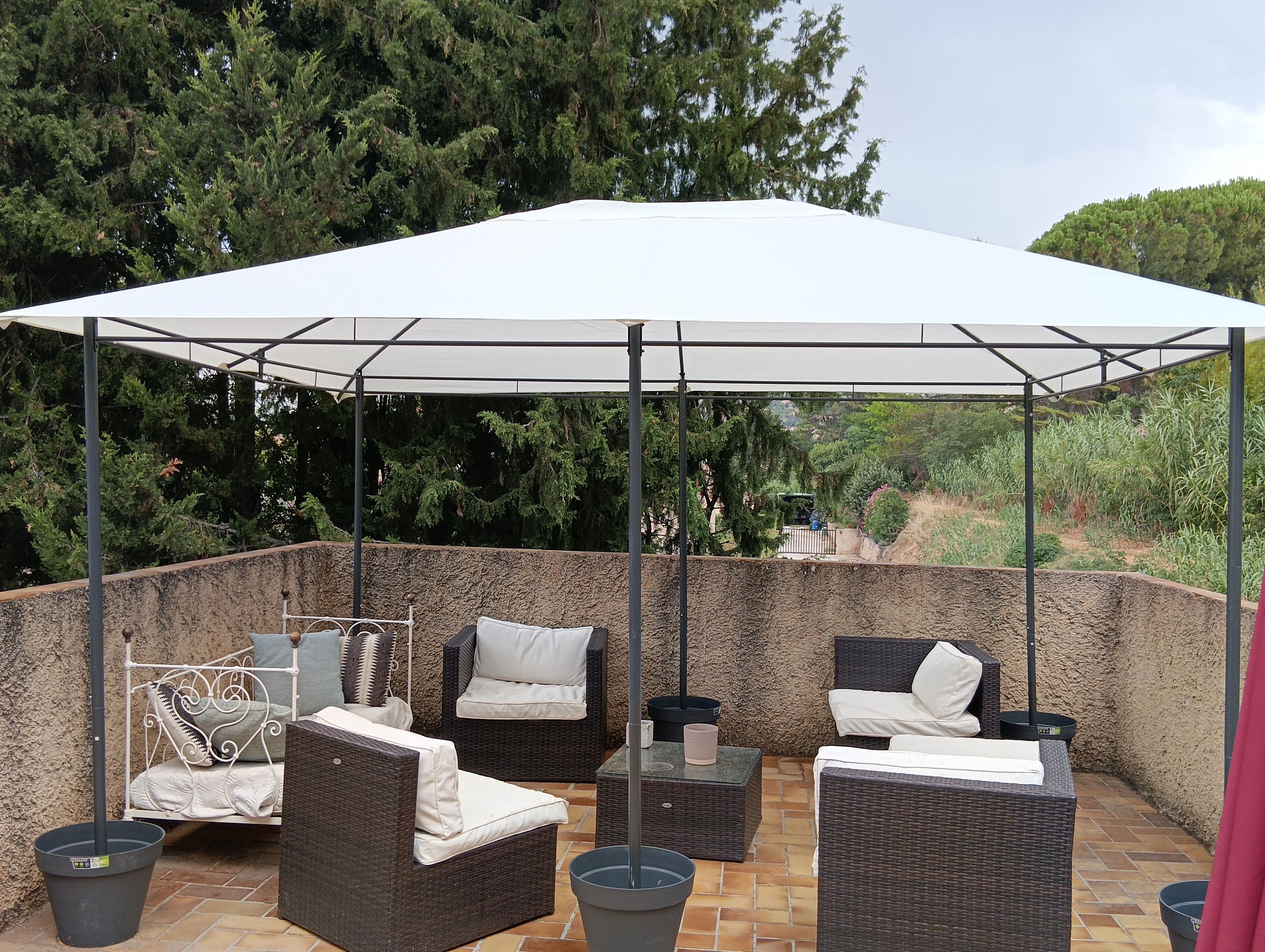 An outdoor patio area with wicker furniture, a white canopy, and a stone wall backdrop.