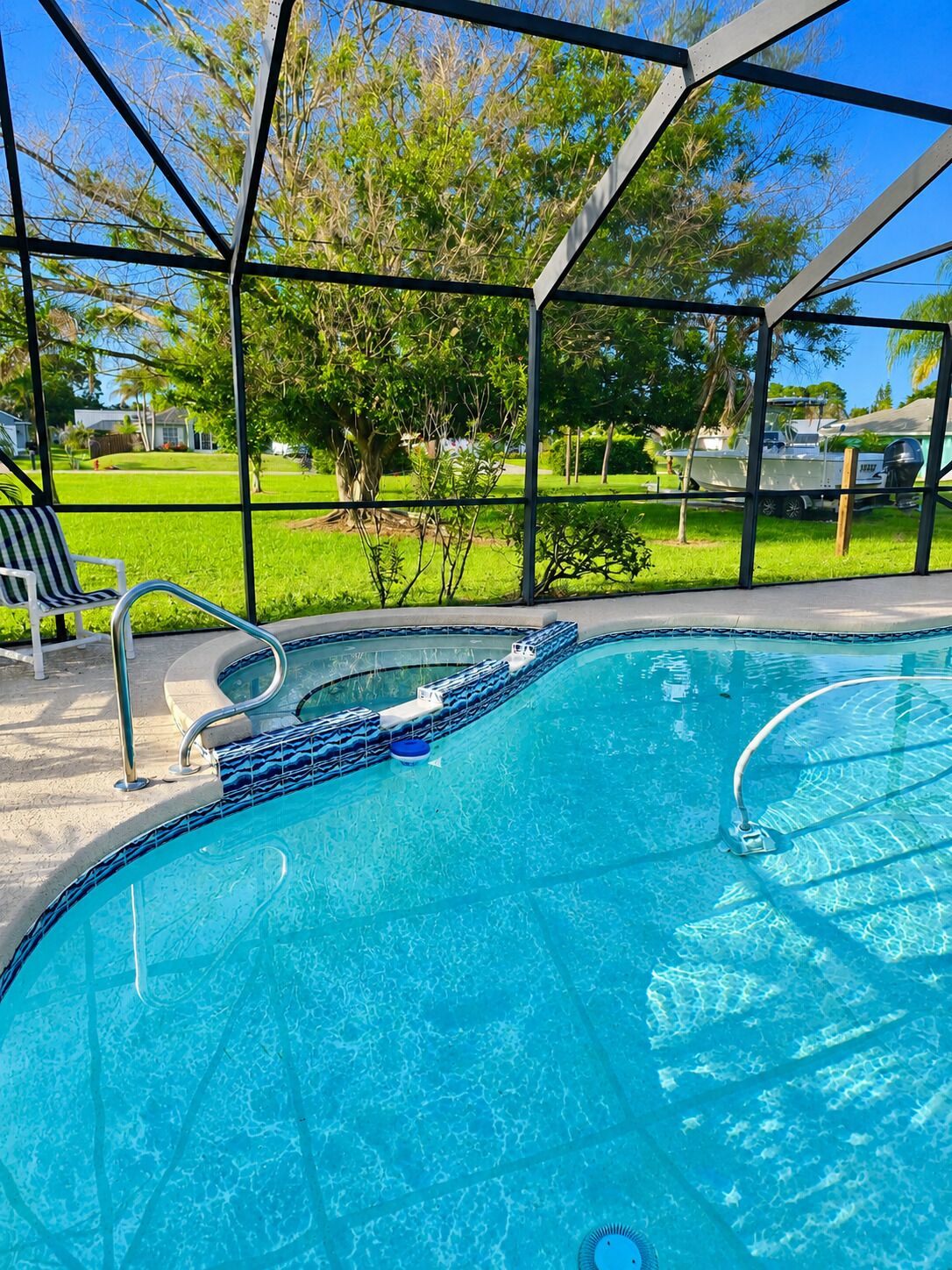 A swimming pool with a metal frame, clear blue water, and a view of a green lawn and trees.