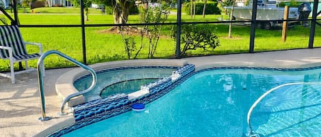 A swimming pool with a metal frame, clear blue water, and a view of a green lawn and trees.