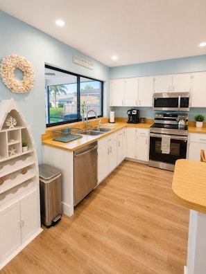 A modern kitchen with white cabinets, stainless steel appliances, a wooden countertop, and a view of the outside. - Casa Azul - 4Br/2Ba Pool & Spa Home, Sleeps 10 (Port St. Lucie)