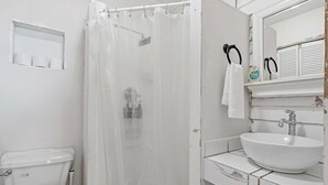 A bathroom with a toilet, a shower curtain, a sink, and a mirror. - Cozy 1BR Near Downtown Lafayette (Lafayette)