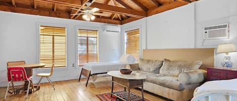 Une pièce avec un plafond en bois, un lit, un canapé, une table à manger avec des chaises et une petite table avec une lampe.