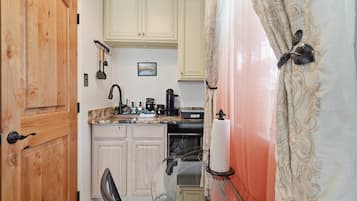 A compact kitchen with wooden cabinets, a countertop with various appliances, and a glass door leading to a bathroom.