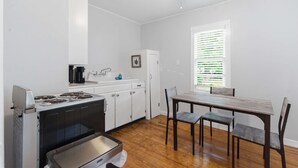 Uma cozinha compacta com fogão, pia e armários, uma mesa de jantar com cadeiras e uma janela com persianas.