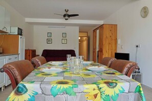 A dining area with a table set for four, a ceiling fan, and a television in the background. - Sunny 3BR Qala home w/Pool & Balcony, WIFI in Gozo (Qala)