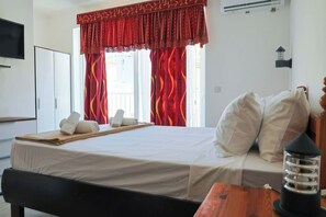 A hotel room with a bed, pillows, a bedside table, a lamp, and a window with curtains. - Sunny 3BR Qala home w/Pool & Balcony, WIFI in Gozo (Qala)