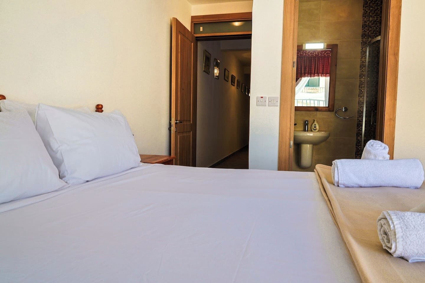 Ein Hotelzimmer mit Bett, Nachttisch aus Holz, Bad mit Waschbecken und Spiegel sowie ein Handtuch auf dem Bett.