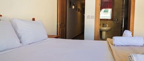 A hotel room with a bed, a wooden nightstand, a bathroom with a sink and mirror, and a towel on the bed.
