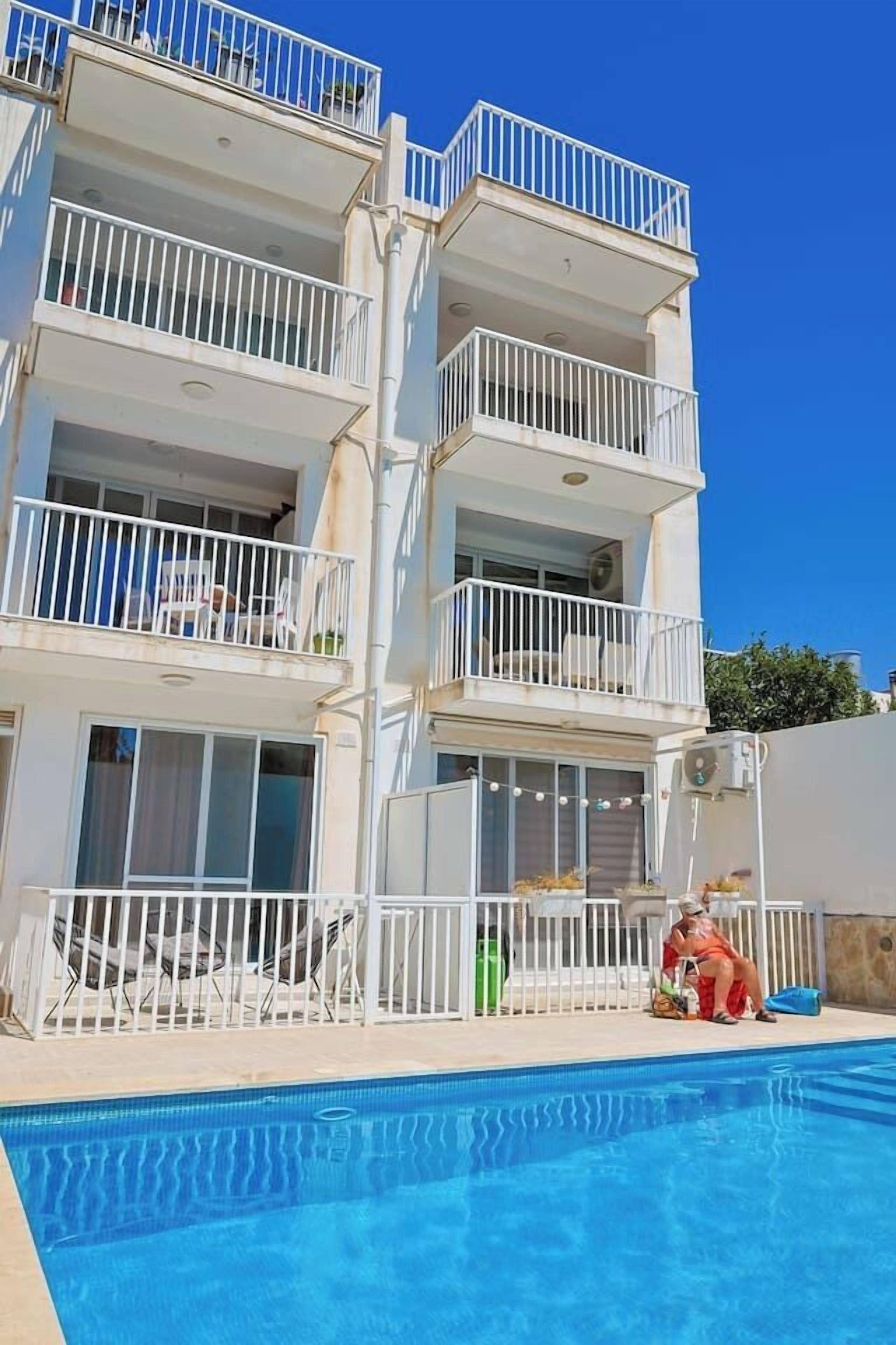 A multi-story building with balconies, a swimming pool, and outdoor seating.