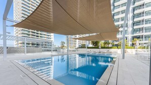 A swimming pool with a clear blue water surface, surrounded by a white tiled deck and shaded by large beige canopies. - Free Housekeeping Visits During Your Stay - Stayshort - Beach Front 2 Bed That Sleeps 6 With Amazing Views (Dubai)