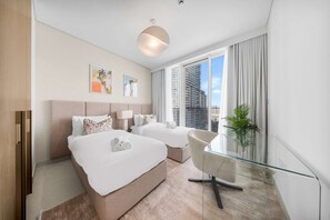 Ein Hotelzimmer mit zwei Betten, einem Glastisch, einem Stuhl, einem großen Fenster mit Blick auf die Stadt und Bildern an der Wand.