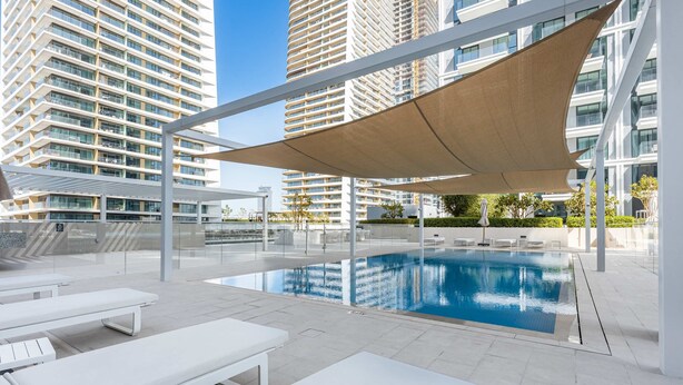 A modern outdoor swimming pool with sun loungers and a shaded area, surrounded by high-rise buildings. - Free Housekeeping Visits During Your Stay - Stayshort - Beach Front 2 Bed That Sleeps 6 With Amazing Views (Dubai)