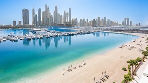 A marina with boats docked, a sandy beach with umbrellas, and a city skyline in the background. - Free Housekeeping Visits During Your Stay - Stayshort - Beach Front 2 Bed That Sleeps 6 With Amazing Views (Dubai)