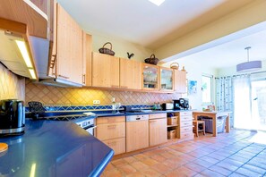A kitchen with wooden cabinets, a blue countertop, and a tiled floor. - Casa Serrao | Carvoeiro | Private Pool & Sea Glimpses | Walk to Dining & Beaches (Carvoeiro)