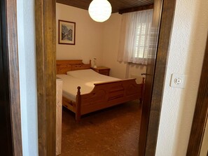 Ein Schlafzimmer mit einem hölzernen Bett, einem Nachttisch, einer Lampe und einem Fenster mit Vorhängen.