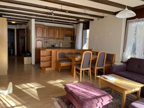 Ein zeitgemäßer Wohnraum mit einem Holzes Esstisch, Stühlen, einer Couch und einer Küche im Hintergrund.