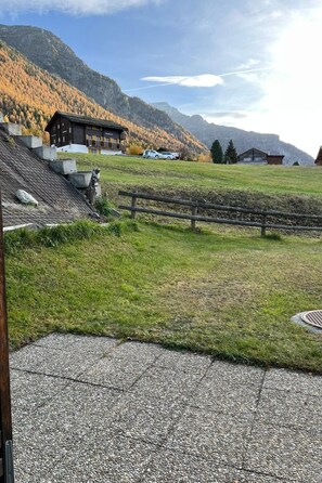 Ein Kiesweg führt zu einem Gebäude mit einem geneigten Dach, umgeben von einer Wiese, mit einem Berg im Hintergrund.