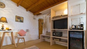 Een knus ingerichte kamer met houten plafond, een televisie, een minibar en opbergplanken.