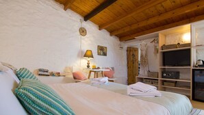 Een slaapkamer met een bed, kussens, een tafel met een lamp, een televisie en opbergplanken.