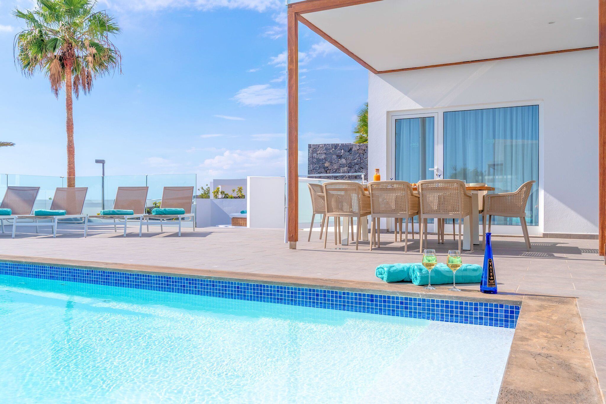 Area piscina con sedie a sdraio e tavolo da pranzo, una palma e cielo sereno.