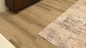 Ein modernes Wohnzimmer mit einem an der Wand befestigten Flachbildfernseher, einer Holz-Unterhaltungseinheit, einem gemusterten Teppich und einer Tür mit Vorhängen.